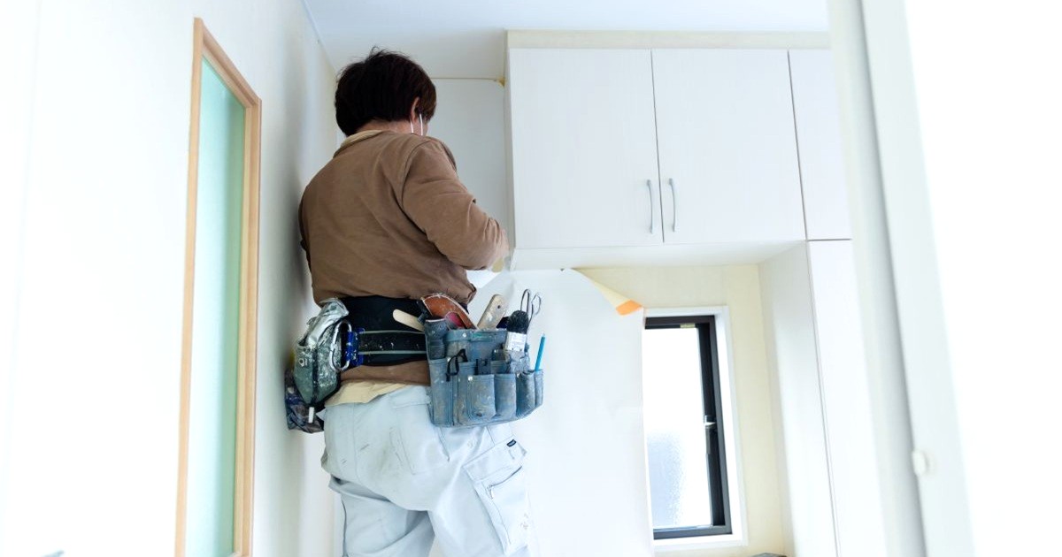 狭小住宅の室内の壁紙を張り替えている職人の男性