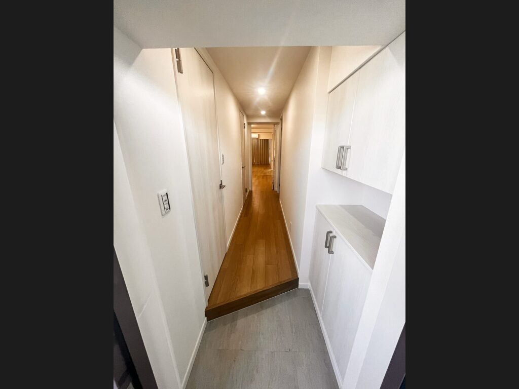 リフォーム後の玄関廊下。白を基調とした明るい内装に造り付け収納、ダウンライトで開放感を演出