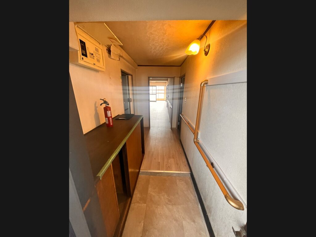 リフォーム前の築年数を感じる玄関廊下。狭い通路に古い下駄箱と手すり、奥に光が差し込む