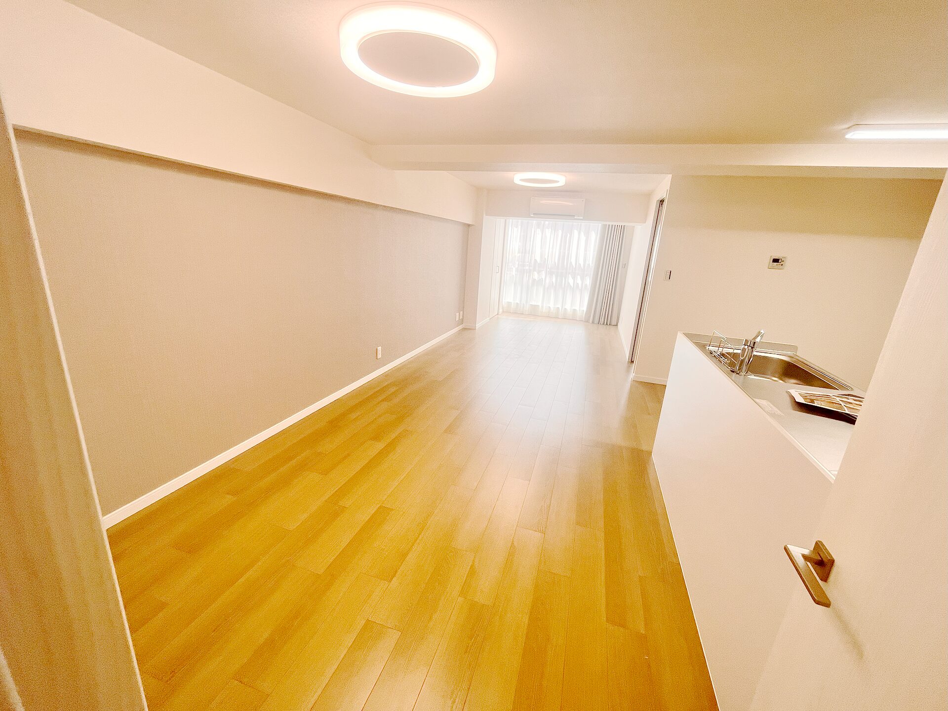 リフォーム後のLDK。対面キッチンへ変更し、白い壁と木目フローリングで明るく広々とした空間に