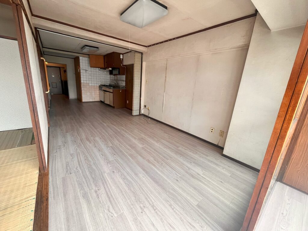 リフォーム前のLDK別角度。経年劣化した壁と古い壁付けキッチン、隣接する和室が見える