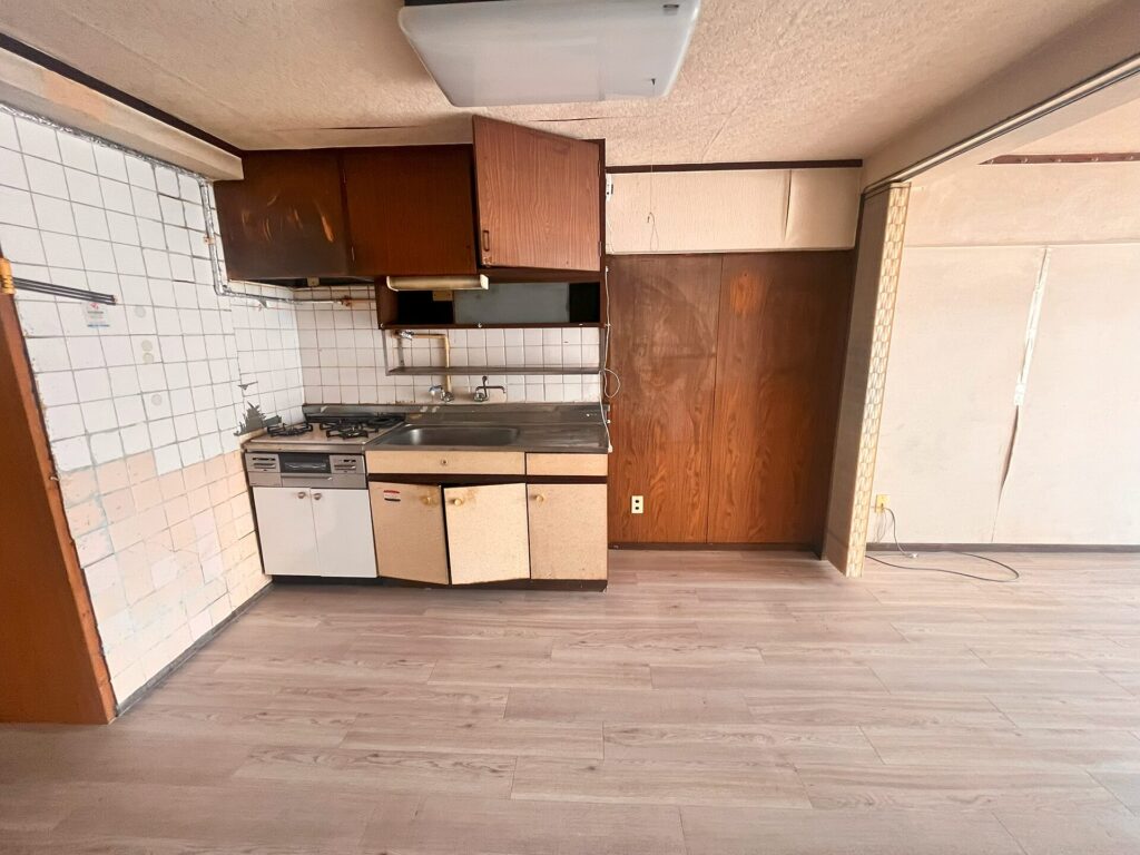 リフォーム前のキッチン正面。古いタイル壁と壁付けキッチン、経年劣化した吊戸棚と収納