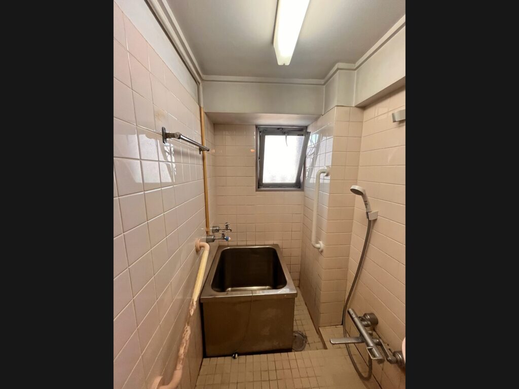 リフォーム前の浴室。古いタイル壁とステンレス浴槽、露出した配管のある在来工法の浴室