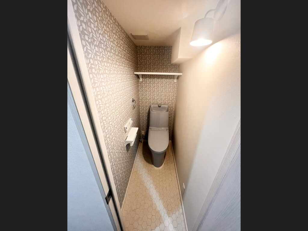 リフォーム後のトイレ。ボタニカル柄アクセントクロスとヘキサゴンタイル床、おしゃれなブラケットライトで空間を演出