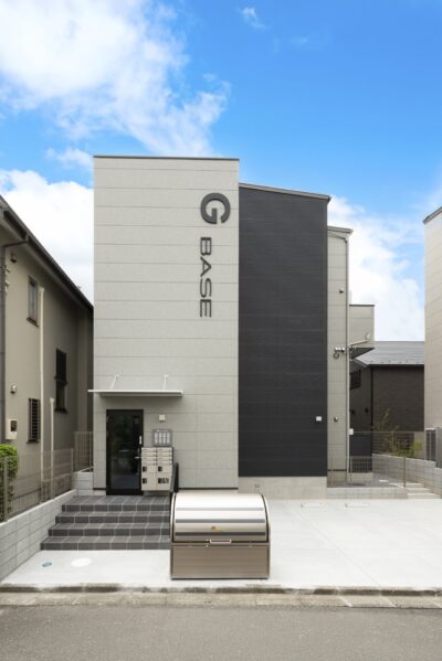 グレーとブラックの外壁に縦書きの館銘板を掲げた2階建ての集合住宅の外観