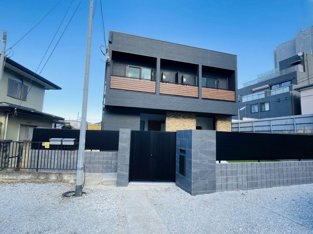 ブラックの門扉と木目調パネルのバルコニーが並ぶ正面外観
